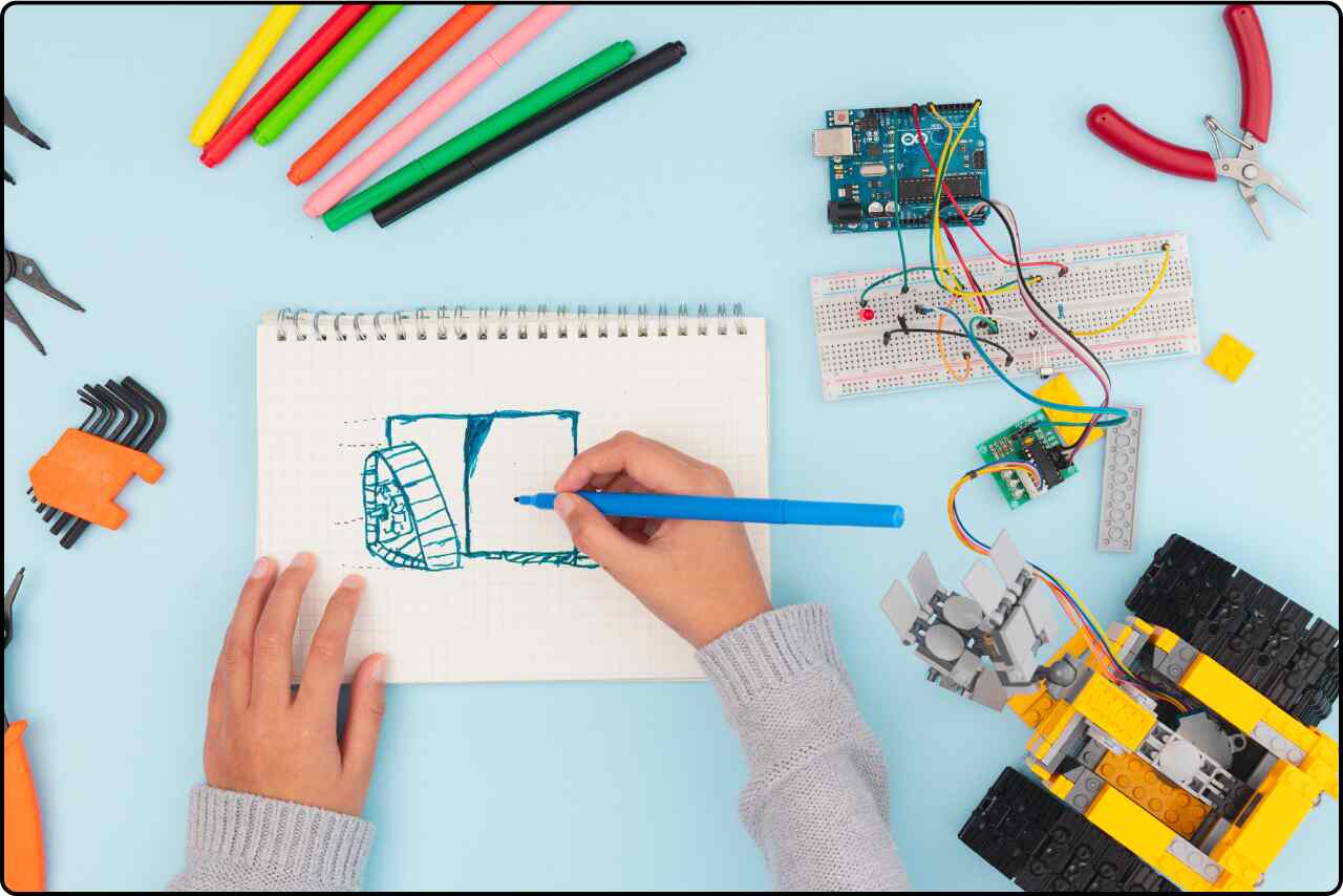 A young boy sketching designs and working on a prototype model on a desk.